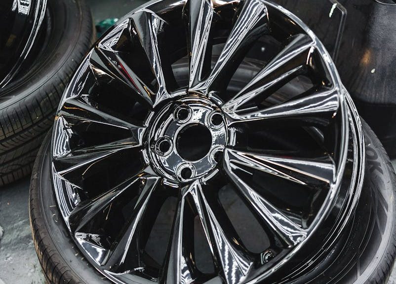 Glossy black car wheel rim and tire stack in an automotive workshop.