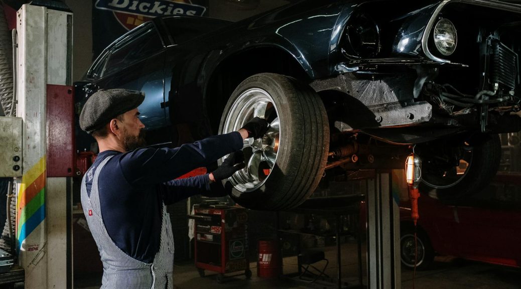 A focused mechanic works on a car wheel in a dimly lit garage, showcasing automotive repair skills.